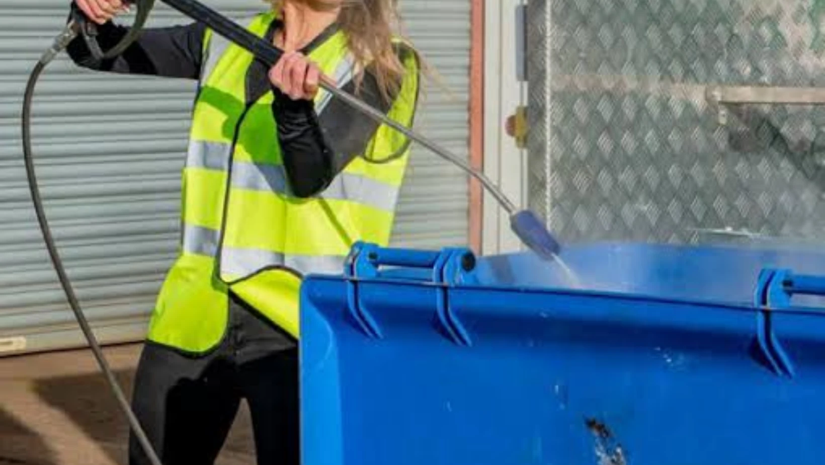 Worker cleaning a blue wheelie bin